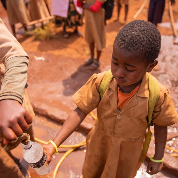 Little african schoolgirl collects water in the bottle from the tap of the fountain